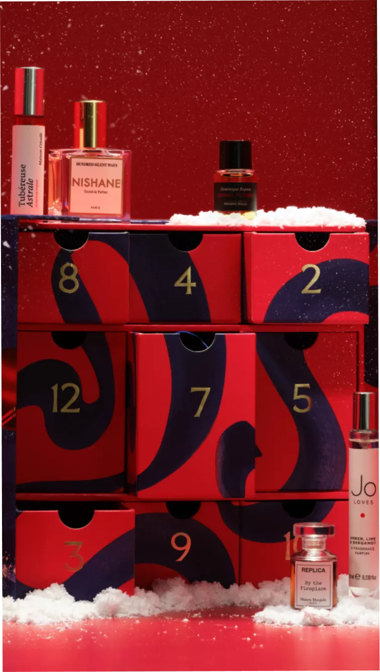 Luxury perfume advent calendar with numbered red drawers, niche fragrance bottles and snow on a festive red backdrop