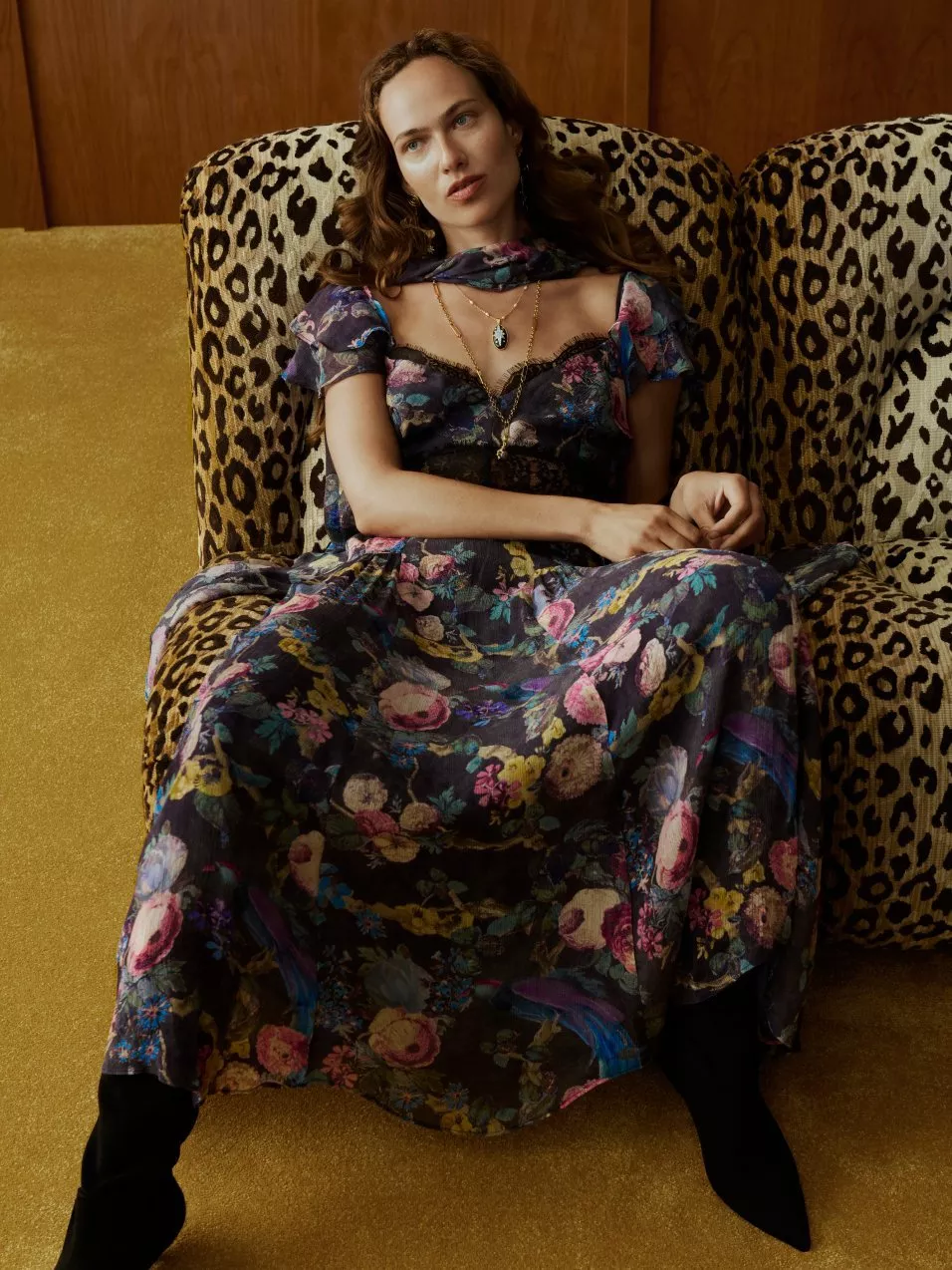 Fashion portrait of woman in floral maxi dress reclining on leopard-print armchair in vintage lounge setting