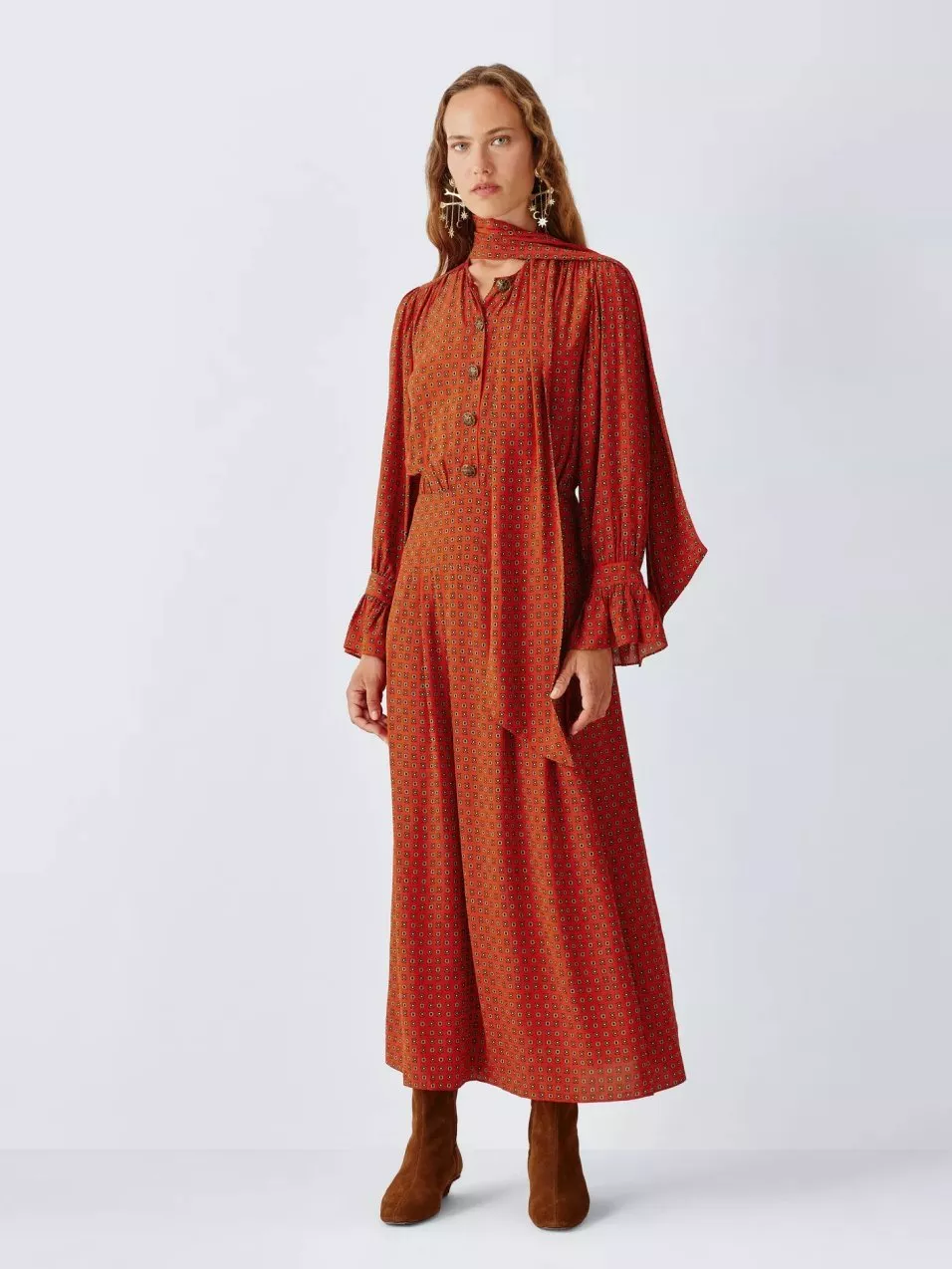 Model wearing red patterned maxi dress with scarf neck, long sleeves and brown ankle boots on white backdrop