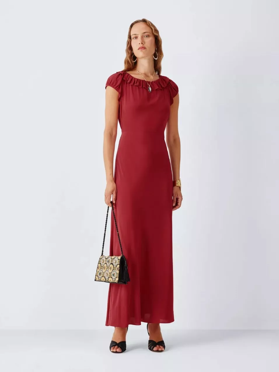 Model wearing a burgundy ruffle-neck maxi dress with cap sleeves, holding a patterned handbag on white backdrop