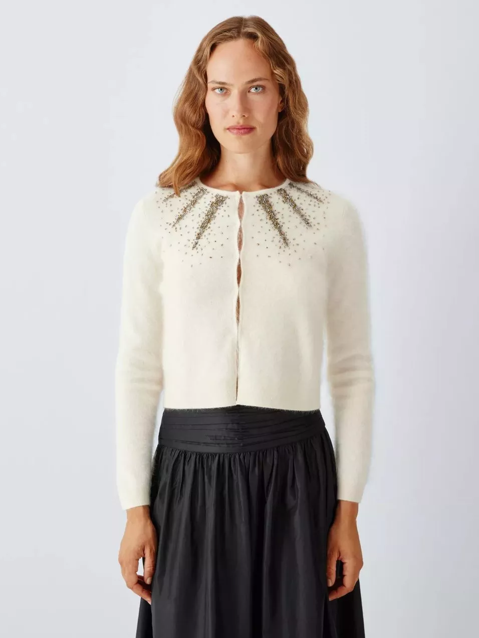 Woman wearing an ivory embellished cardigan with beaded neckline, styled with a black high-waist skirt, studio shot