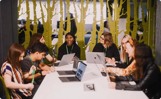 Diverse team in modern office meeting room, collaborating at laptops around table with green wall divider.