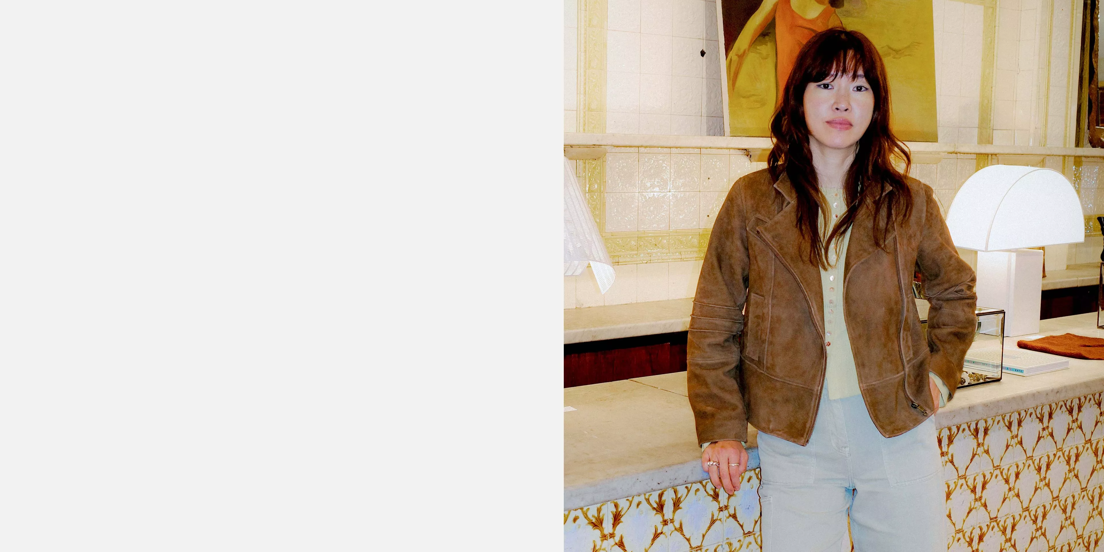 Woman in brown suede jacket and light jeans standing by tiled counter with lamps in a stylish boutique interior