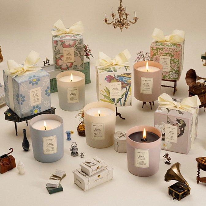 Elegant Jo Malone candles in pastel glass jars are surrounded by floral gift boxes and miniature vintage decor, creating a whimsical and luxurious display.