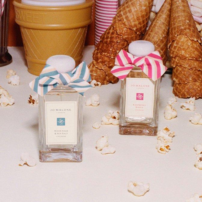 Jo Malone colognes with striped bows (blue and pink) are displayed among popcorn, waffle cones, and ice cream cups, creating a playful dessert-themed setup.