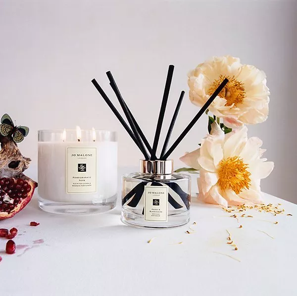 Jo Malone scented candle and diffuser with black reeds, pomegranate and white peonies on a minimalist table.