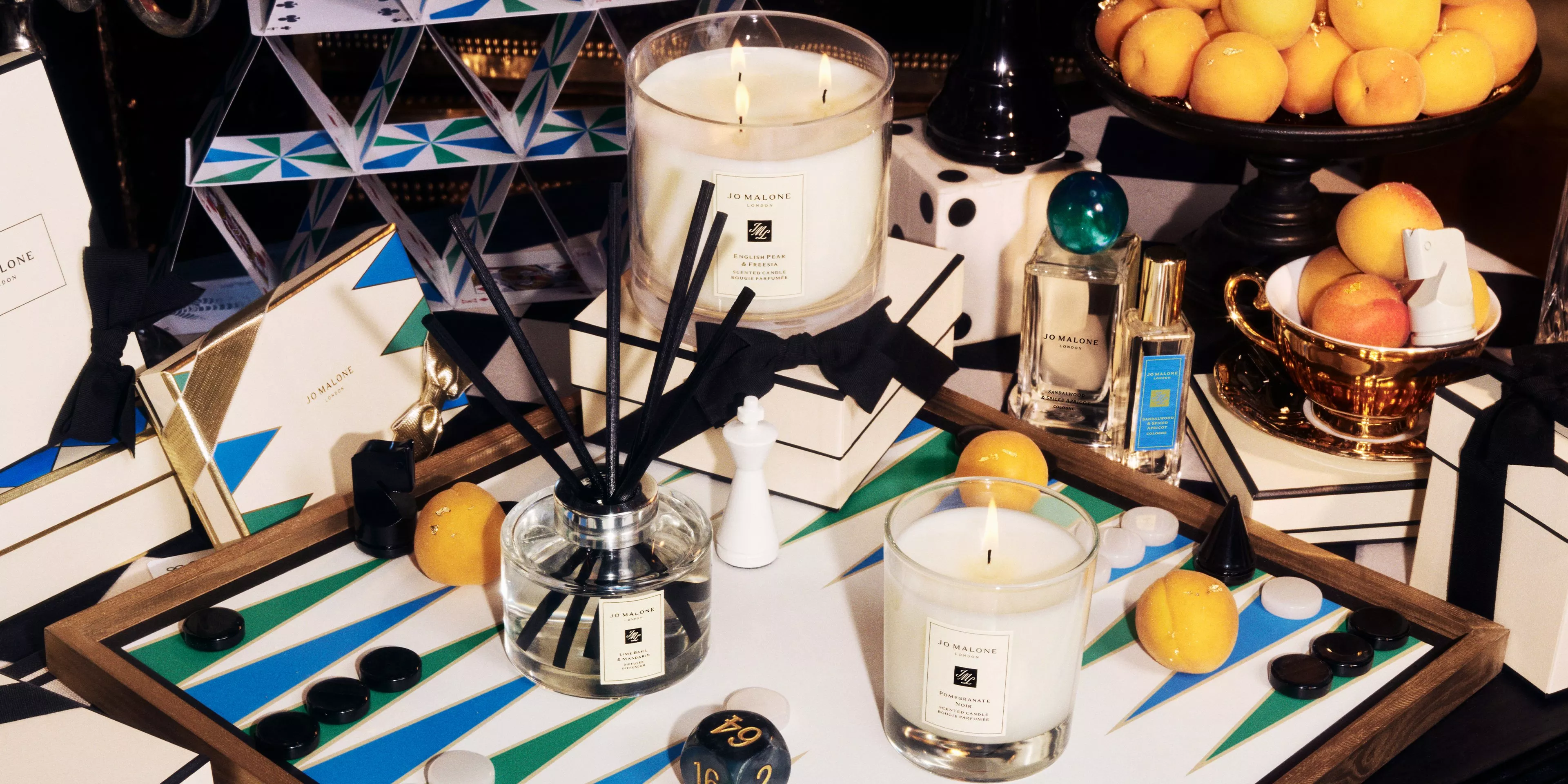 jo malone candles, diffuser, and fragrance bottles on a table with board games