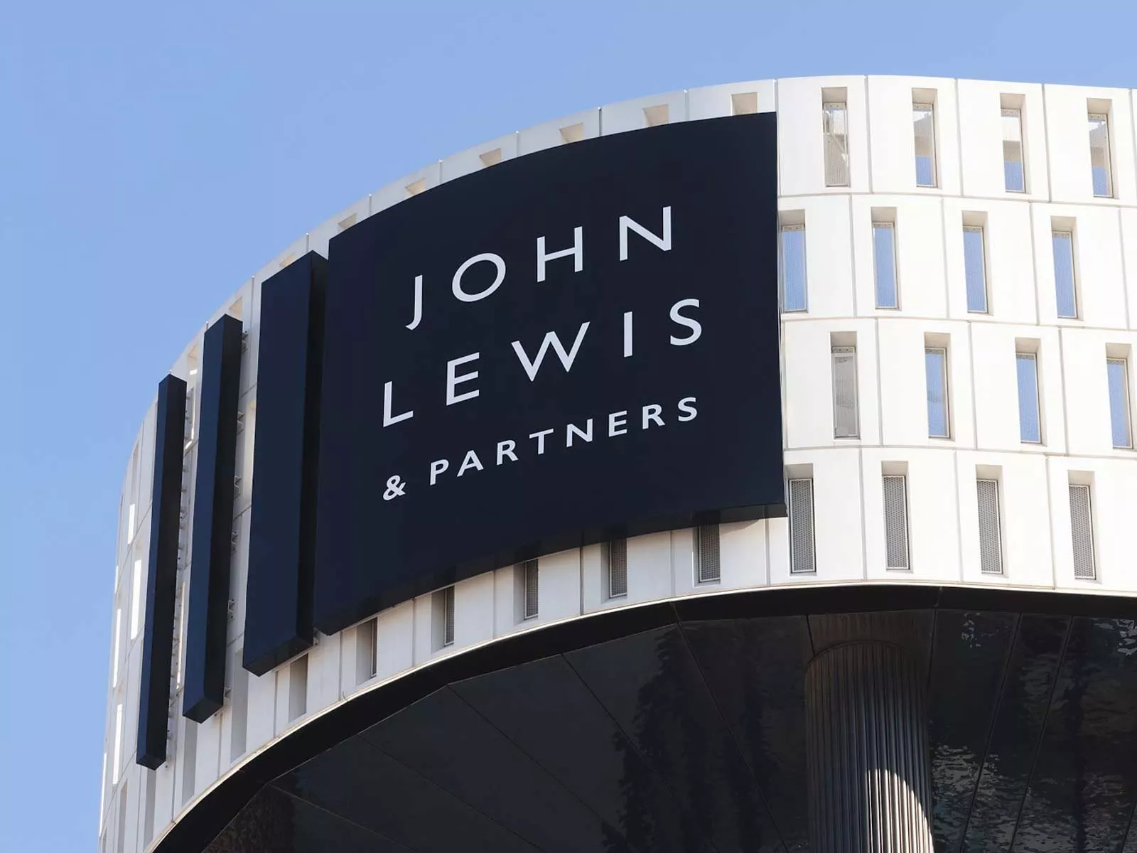 John Lewis & Partners sign on modern curved department store building exterior against clear blue sky