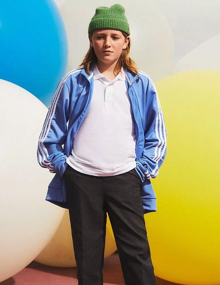 Boy wearing green beanie hat, blue adidas tracksuit jacket over a school uniform white polo top and dark grey trousers