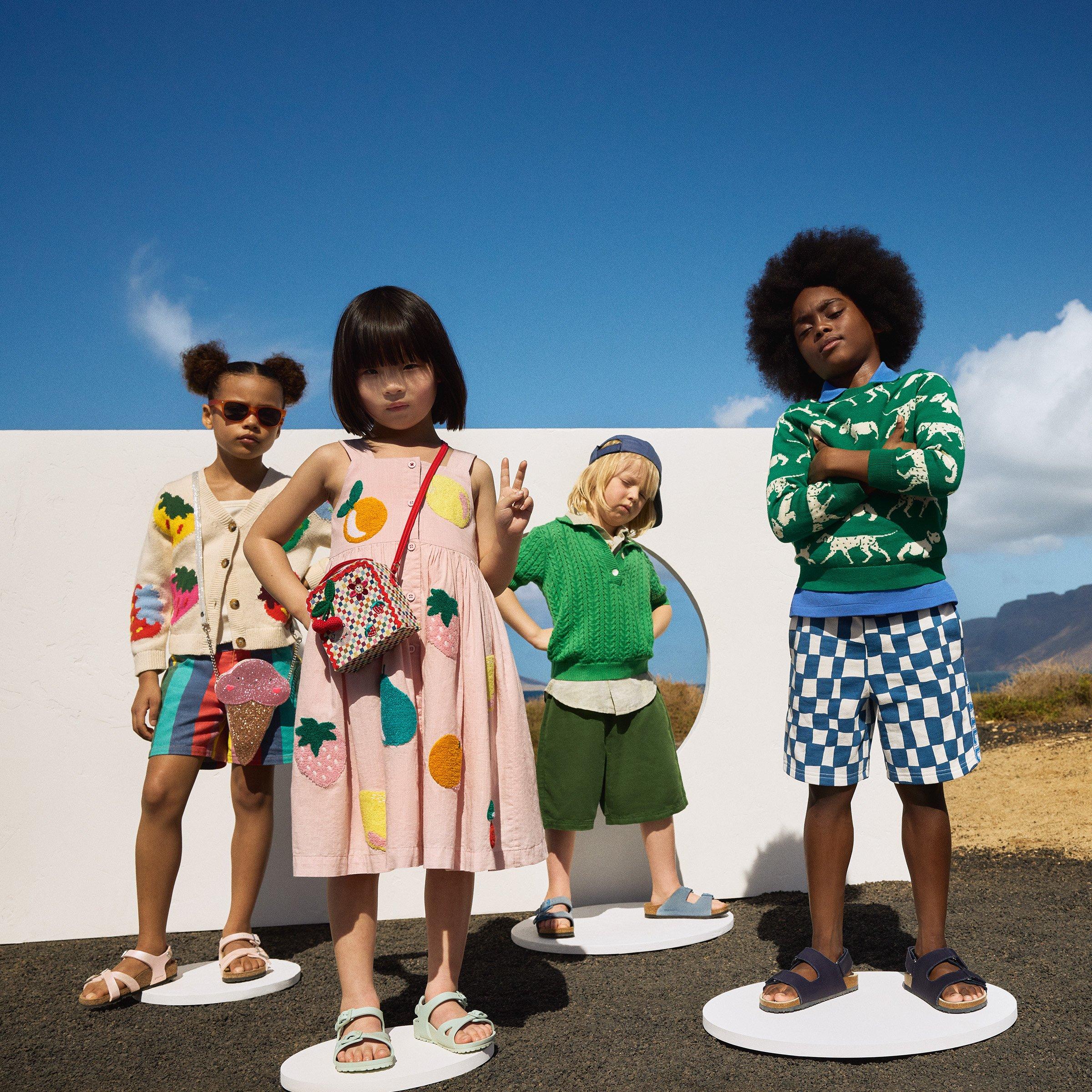 Four stylishly dressed children pose confidently on circular platforms outdoors against a blue sky, showcasing colorful and playful summer outfits