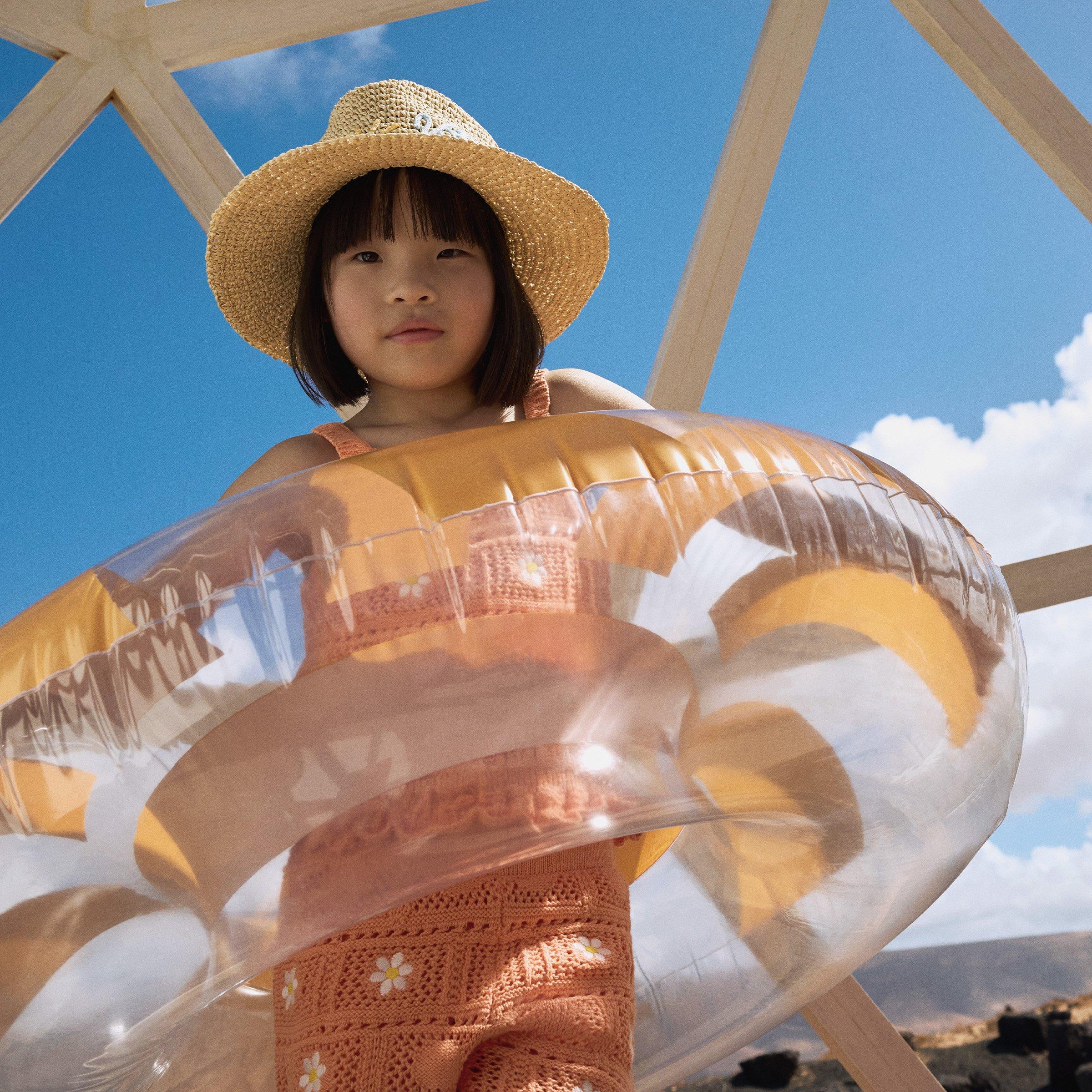 A girl wearing a hat and swiming tube with blue sky in baground
