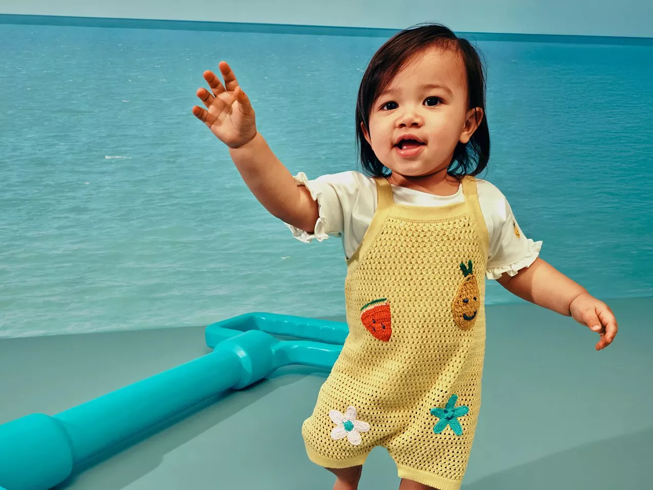 Baby in knitted yellow jumpsuit with fruit and sea creatures on.