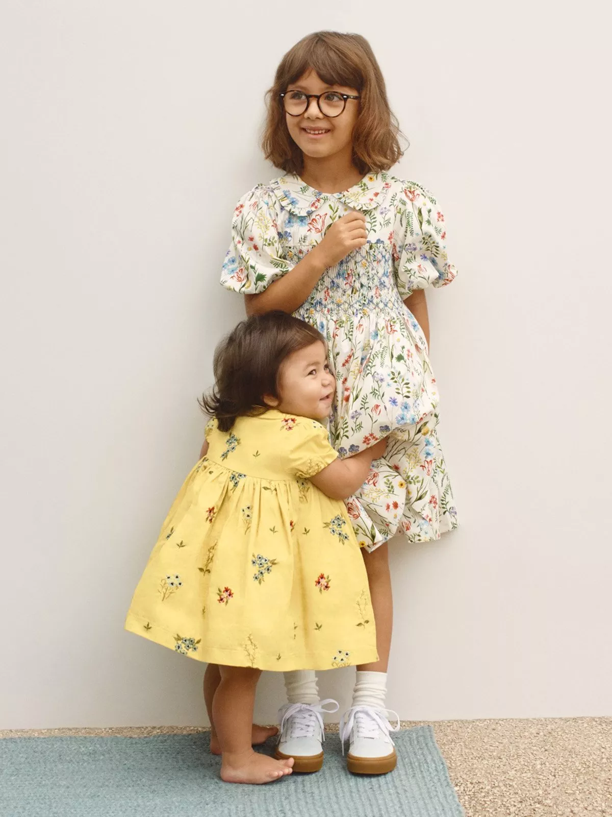 Girl in floral white wedding outfit. Toddler in yellow floral wedding outfit. Hugging eachother