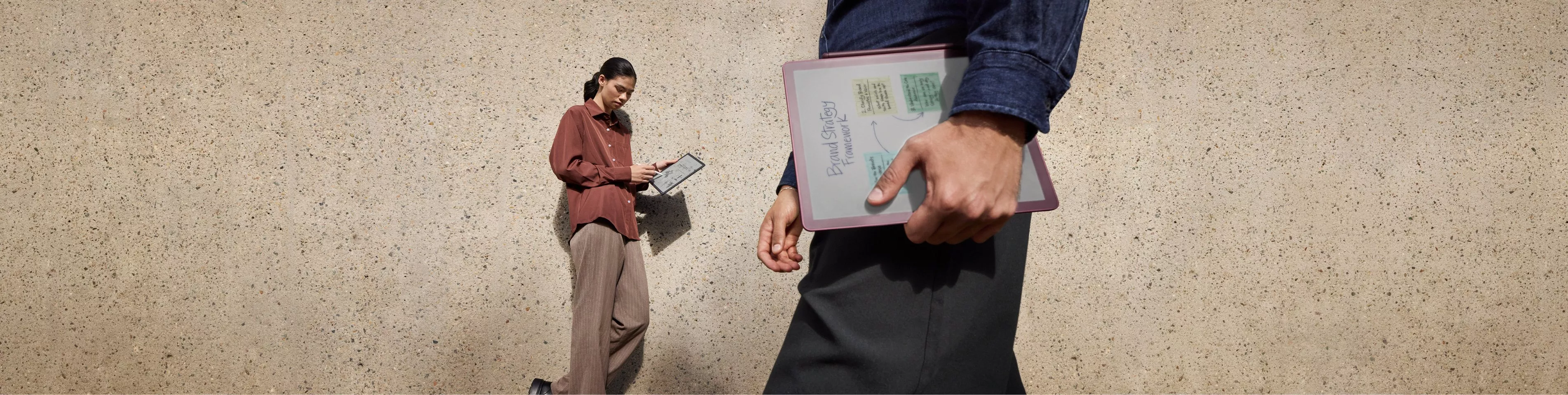 A woman using a Kindle Scribe while sitting at a wooden desk, surrounded by motion-blurred crowds.