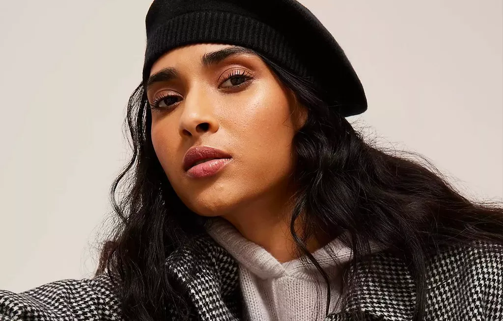Close-up fashion portrait of woman in black beret and houndstooth coat, showcasing autumn style and makeup.