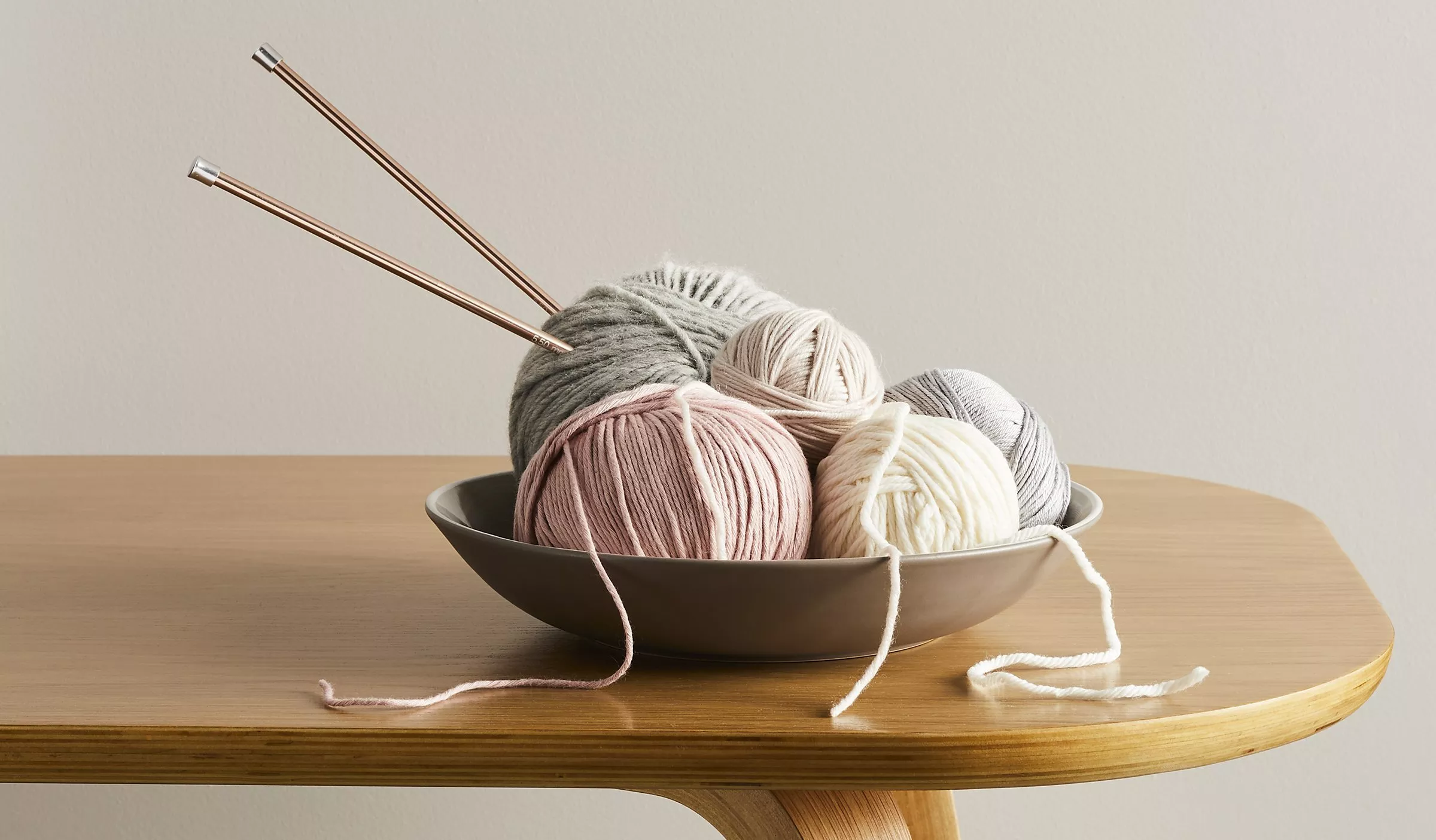 A bowl with different coloured yarn and a pair of knitting needles 