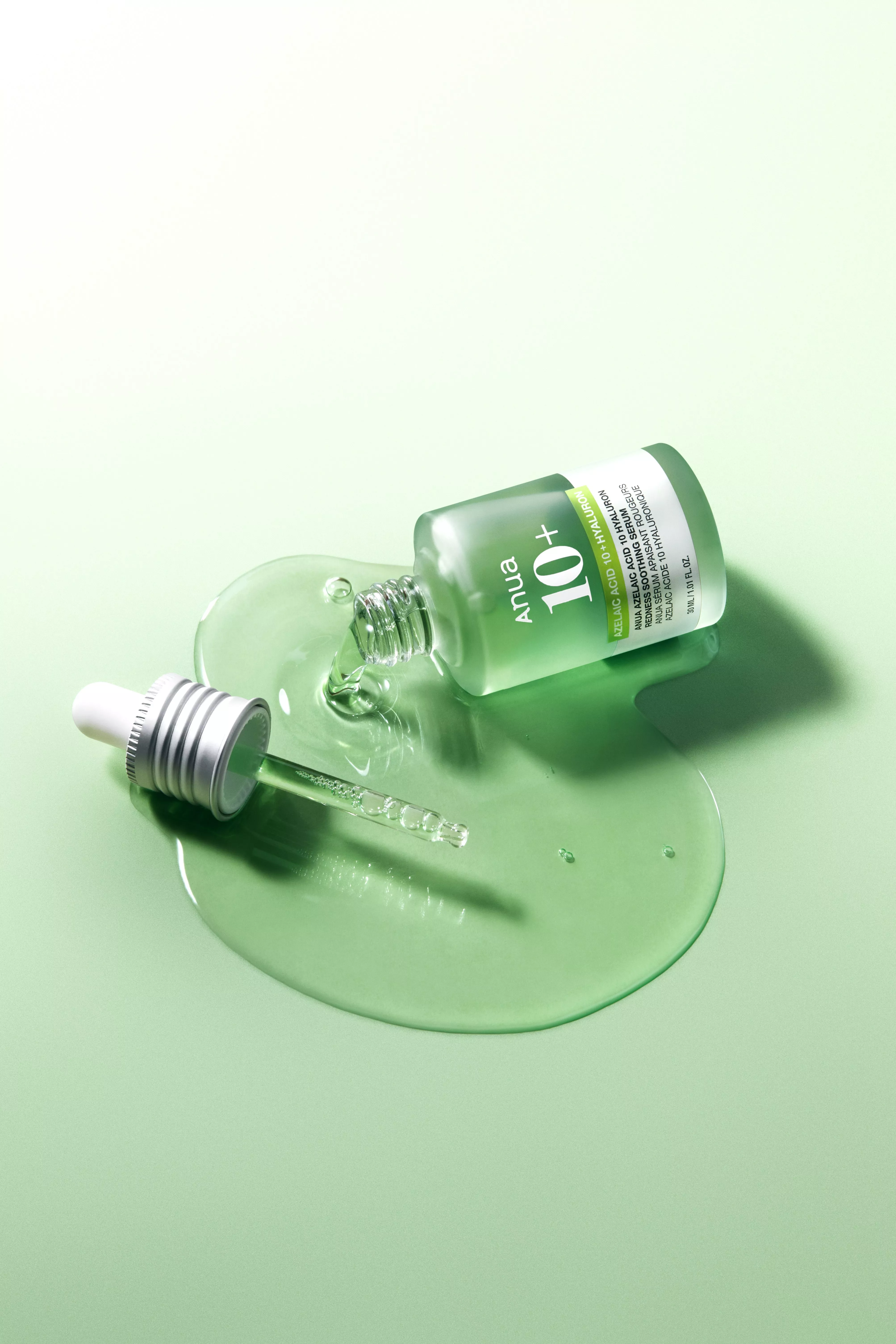 Anua 10+ azelaic acid and hyaluron serum bottle with dropper, spilled green skincare liquid on pastel background