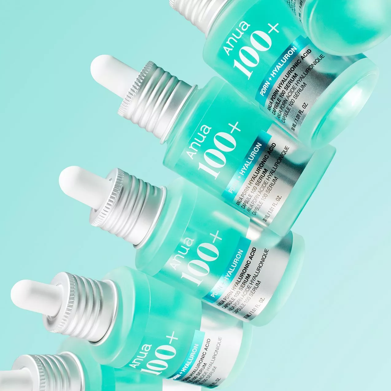 Anua 100+ PDRN and hyaluronic acid serum dropper bottles arranged on a pastel aqua background.
