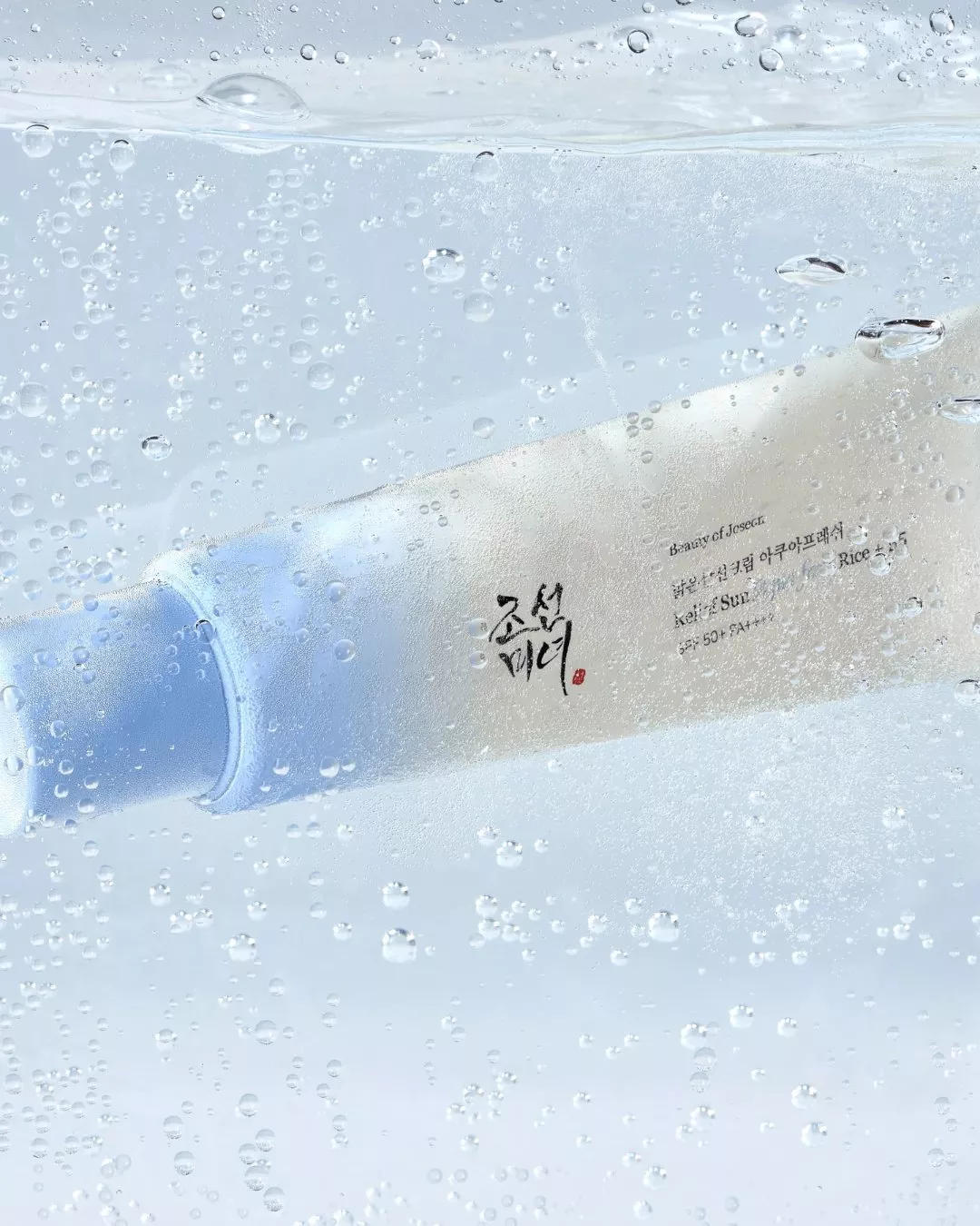Beauty of Joseon sunscreen tube underwater with bubbles, Korean SPF50+ skincare product close-up on blue background
