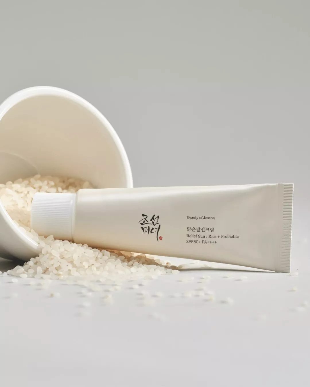 Beauty of Joseon Relief Sun SPF50+ sunscreen tube beside spilled rice grains on a grey background