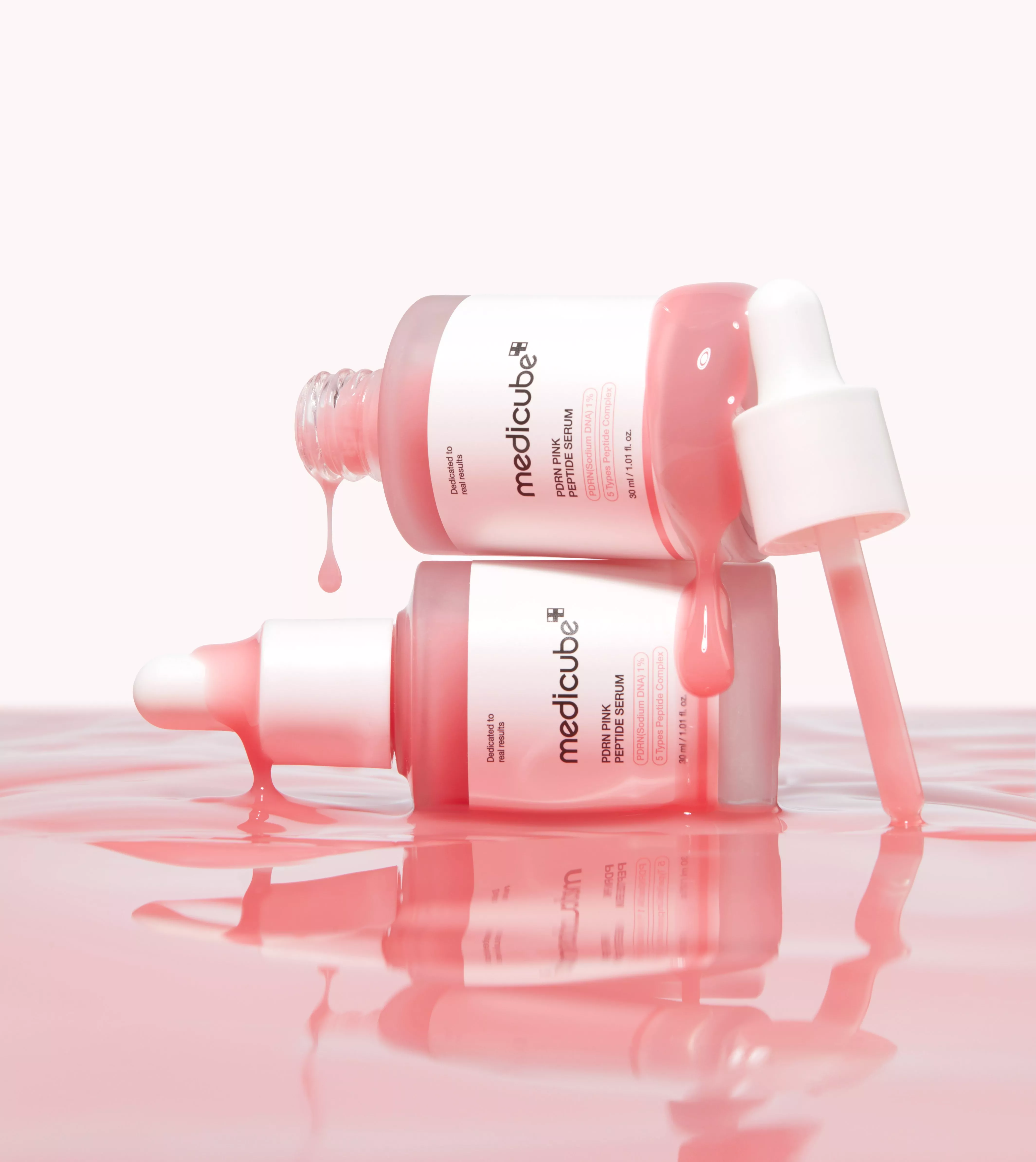 Medicube PDRN Pink Peptide Serum bottles with droppers, pink serum dripping on glossy surface reflection
