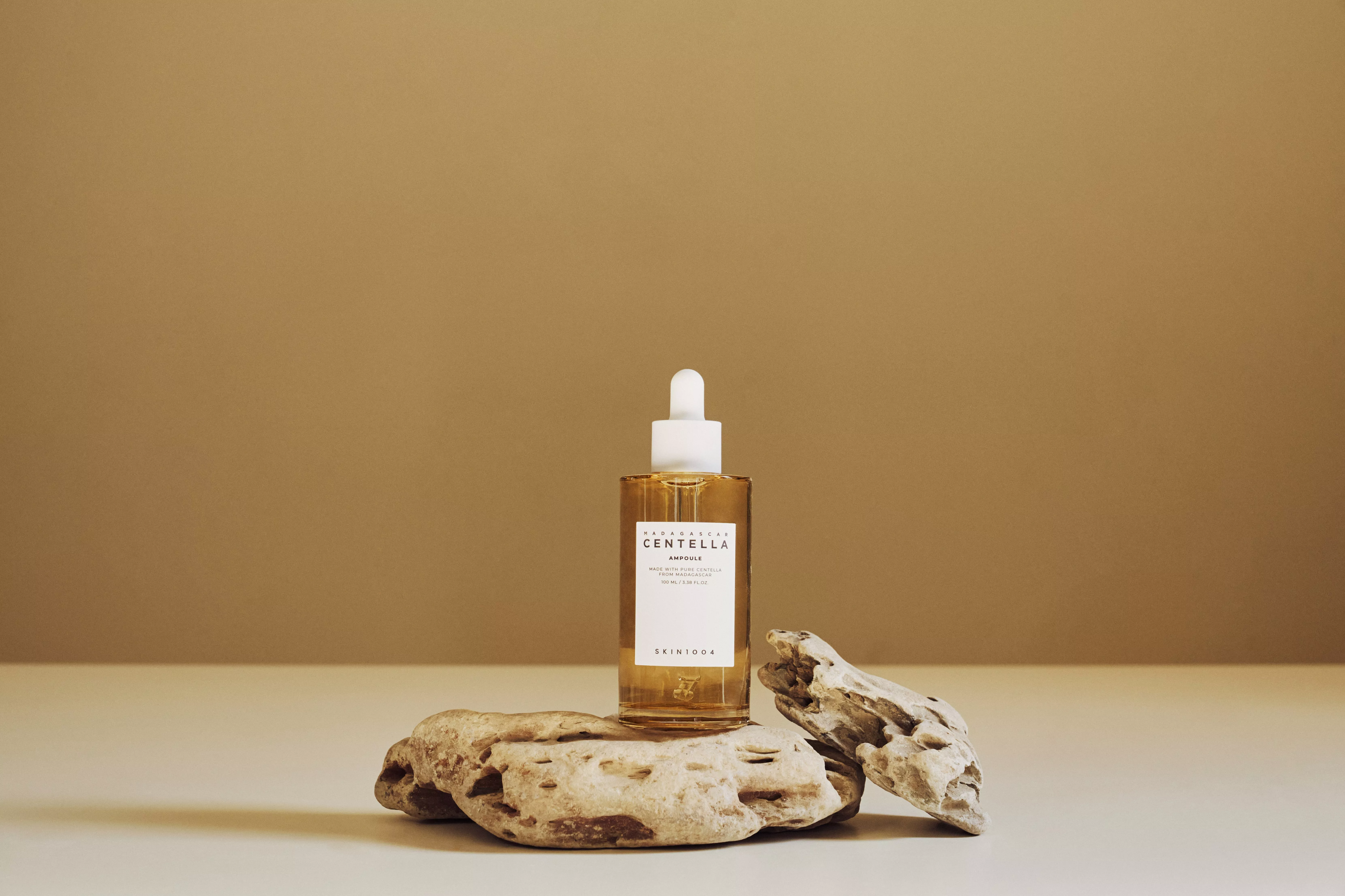 Centella ampoule skincare serum dropper bottle on natural stones against a warm beige background, product photo