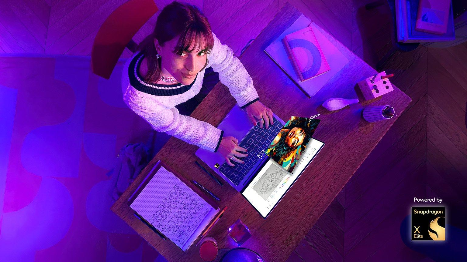 Overhead view of woman sitting at desk with laptop, looking up