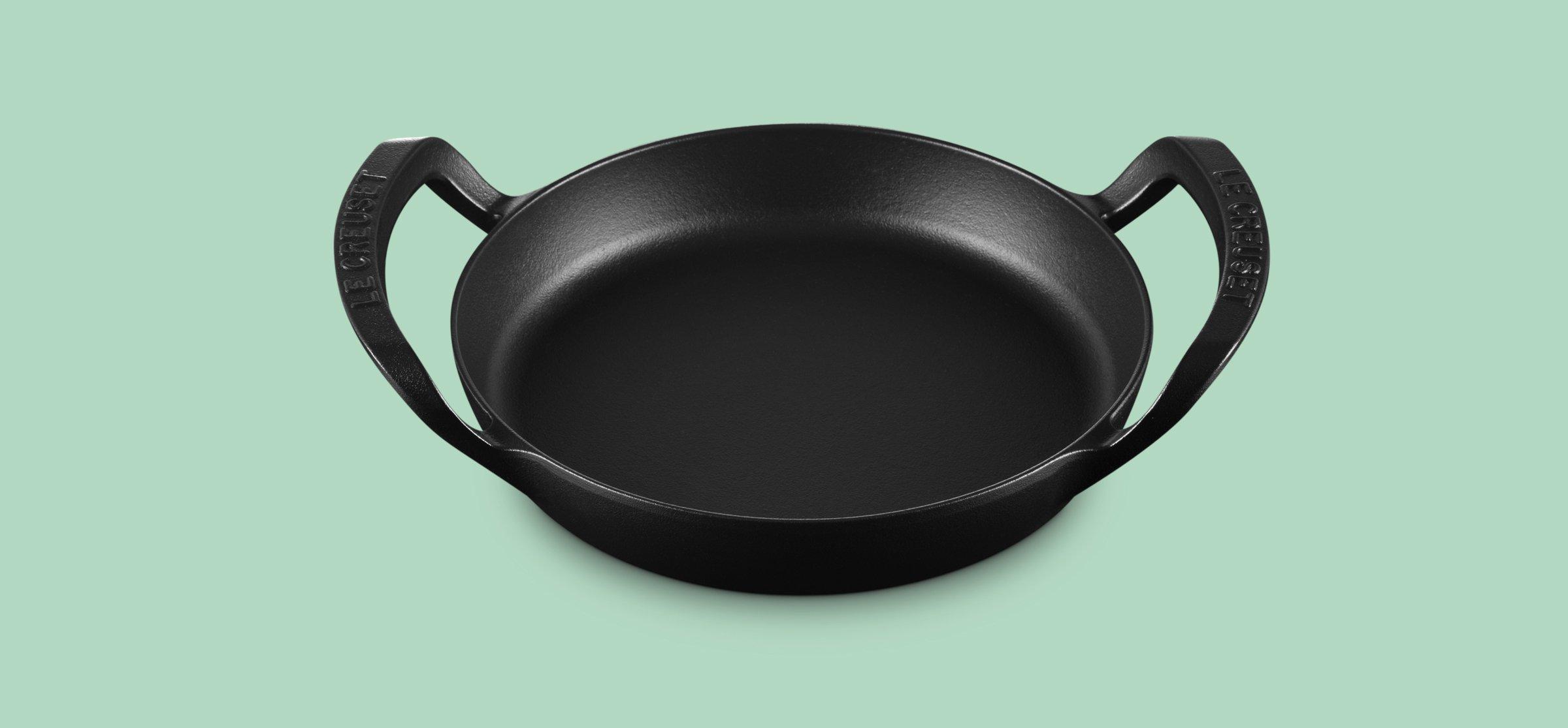 A black Le Creuset skillet on a green background