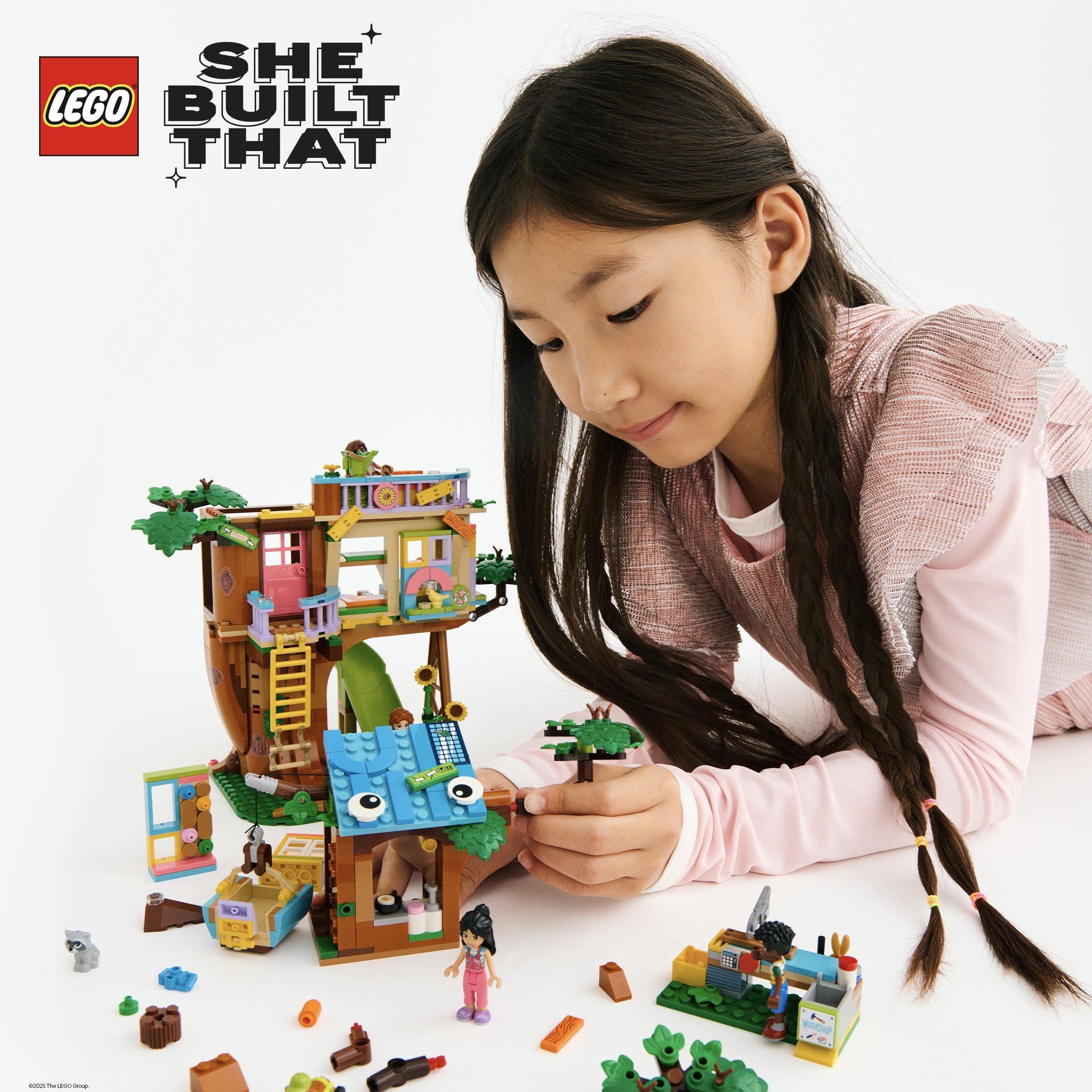 A young girl playing with a colorful LEGO treehouse set, surrounded by mini figures and accessories.