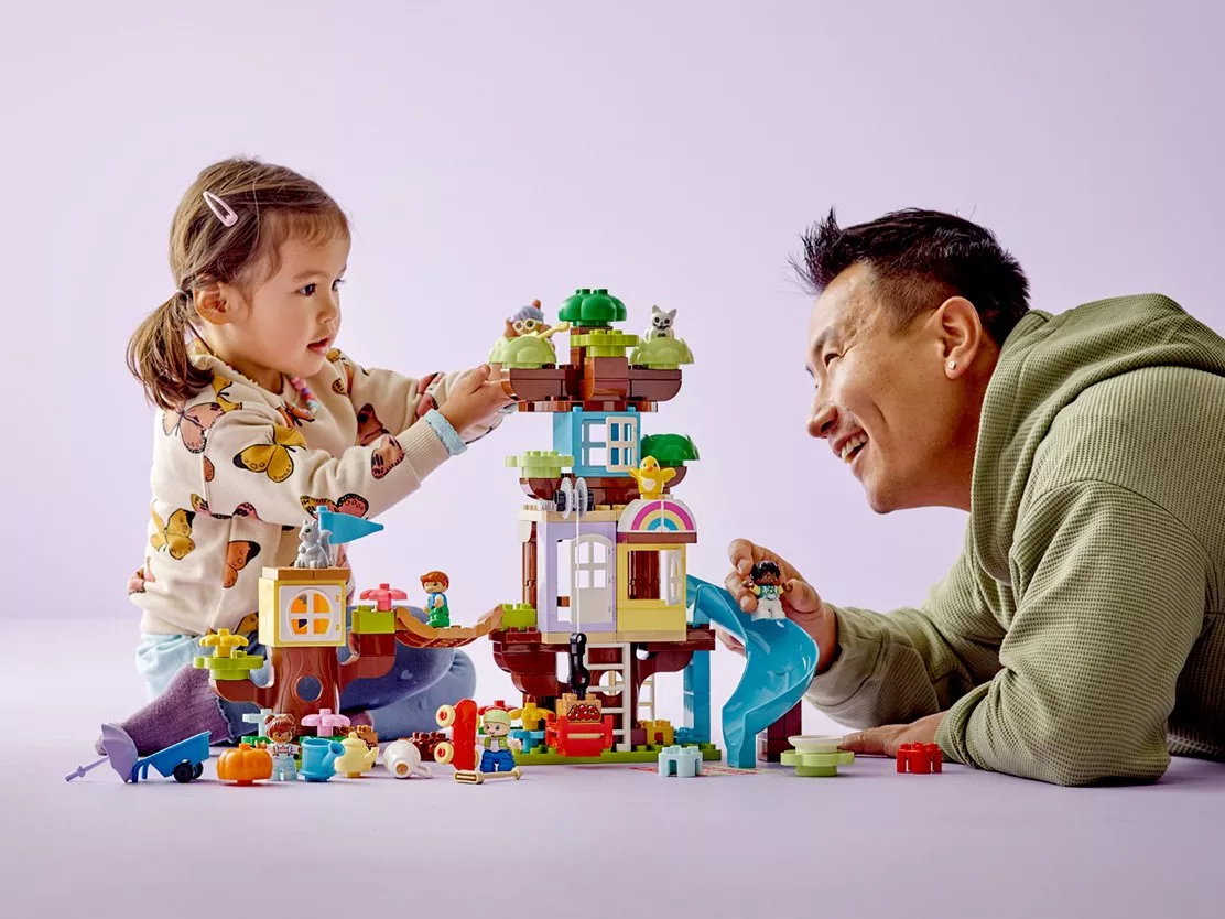 girl playing with a tree house lego set with her dad