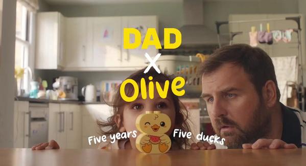 Dad and daughter Olive peeking over table with cute duck toy, playful family moment in cosy kitchen setting
