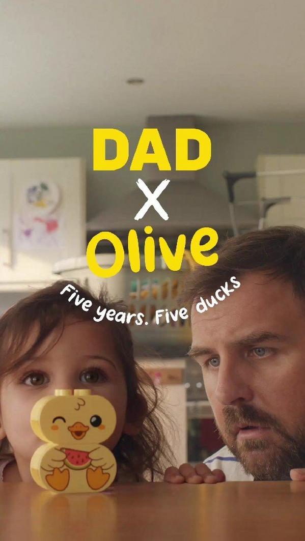 Dad and daughter Olive peeking over table with cute duck toy, playful family moment in cosy kitchen setting