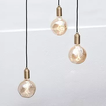 Three hanging vintage Edison filament bulbs with brass holders on black cords against a white wall background