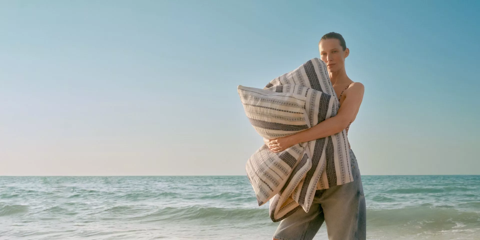 Woman holding striped beach towel by the sea at sunset, coastal lifestyle and summer holiday travel concept