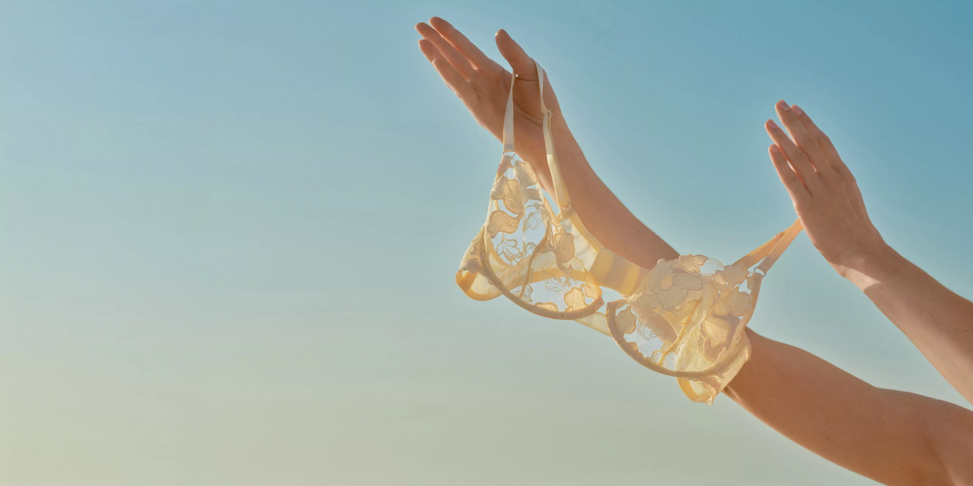 hands of a person holding up a summery bra up to the blue sky