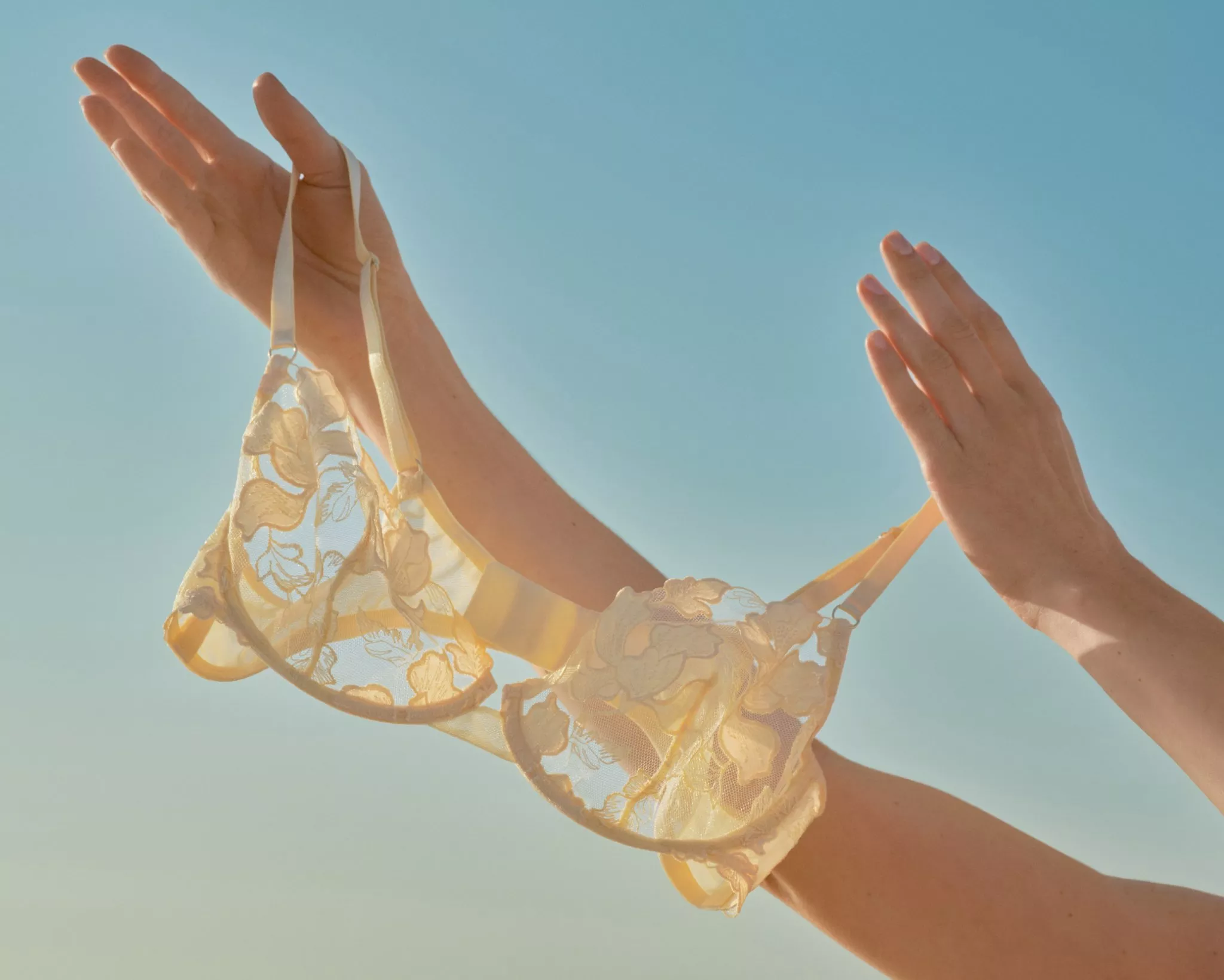 hands of a person holding up a summery bra up to the blue sky