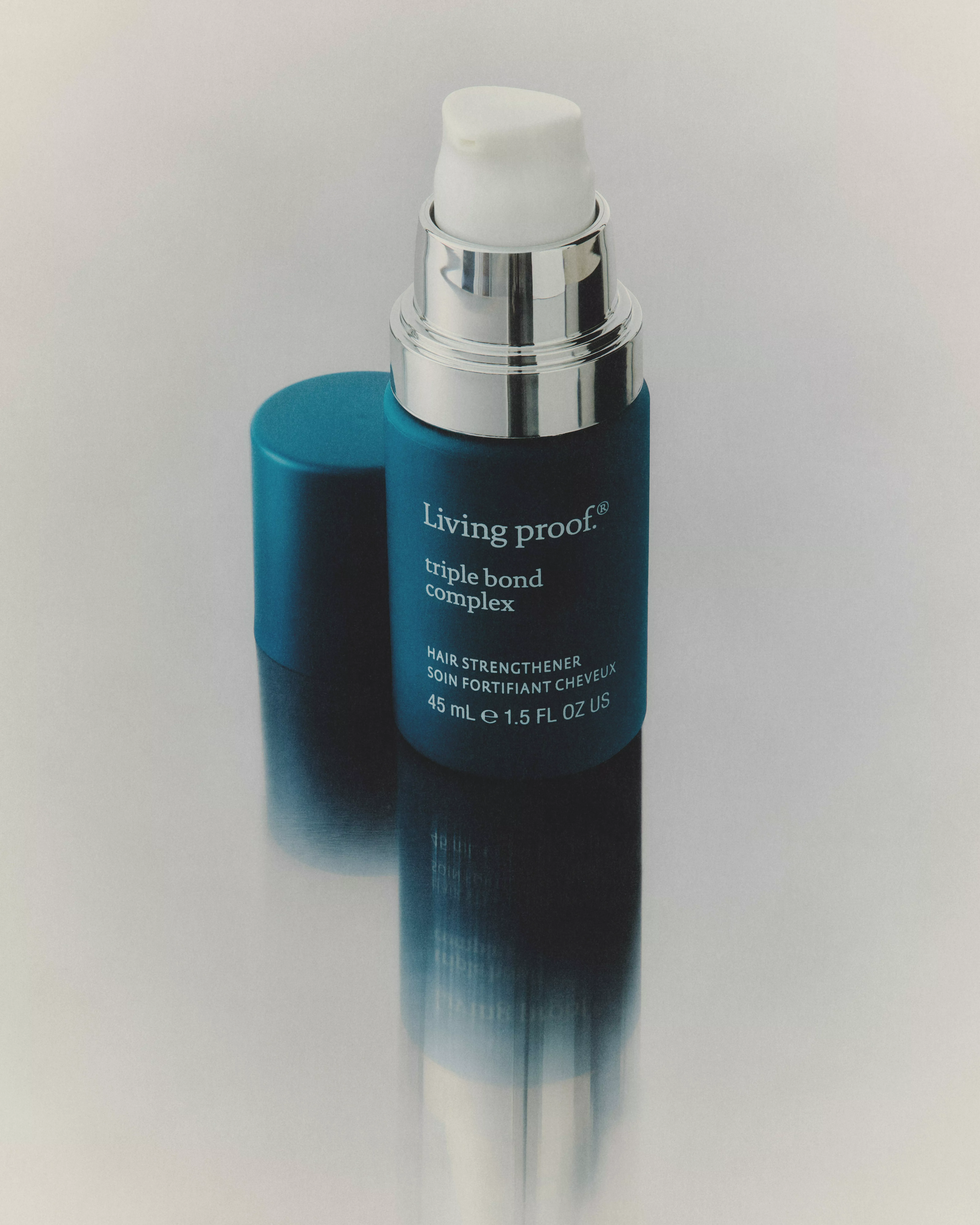 Living Proof Triple Bond Complex hair strengthener bottle with pump and cap on reflective surface background