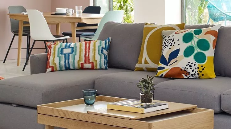 Modern grey corner sofa with colourful cushions and oak coffee table in bright open-plan living room