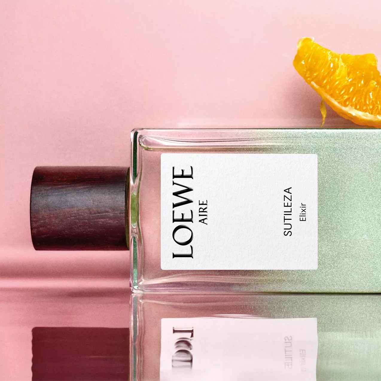 Loewe Aire Sutileza Elixir perfume bottle on a pink background with an orange slice garnish.