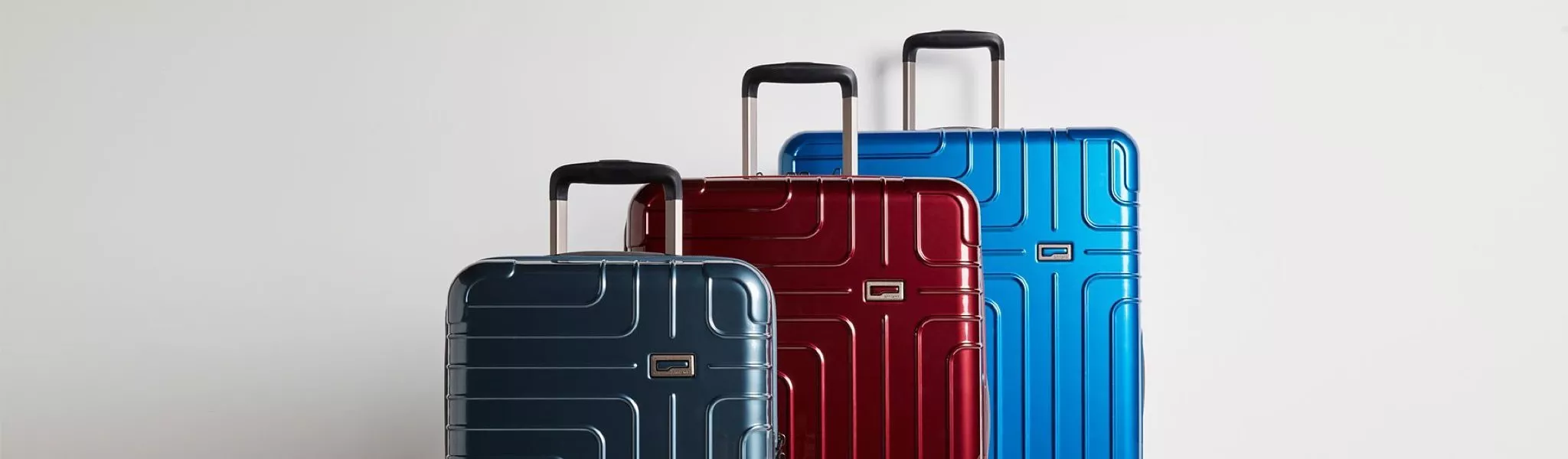 Three hard-shell wheeled suitcases in blue, red and grey with telescopic handles on a light background