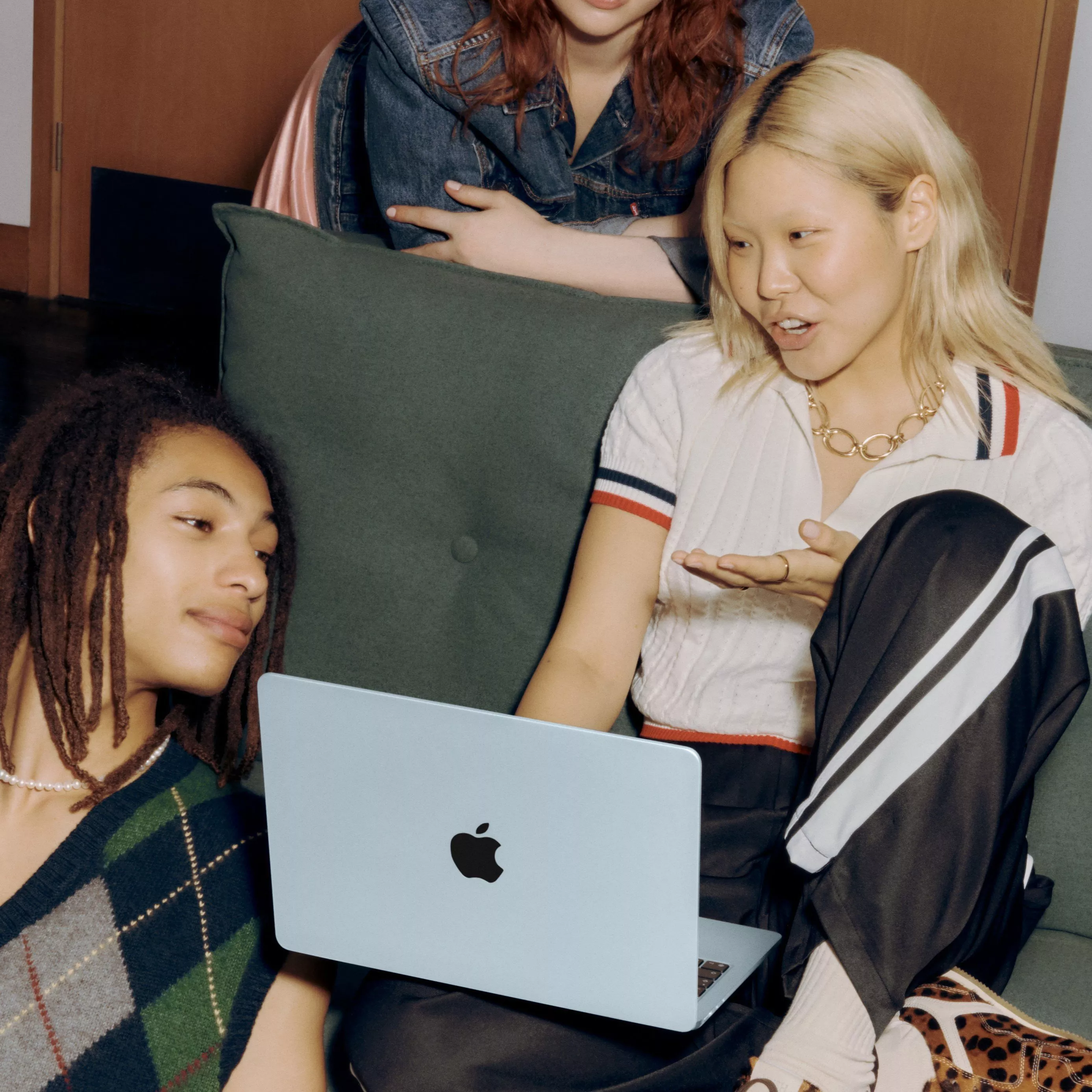 Three individuals are gathered around a blue laptop, sitting on a sofa, engaged in conversation.