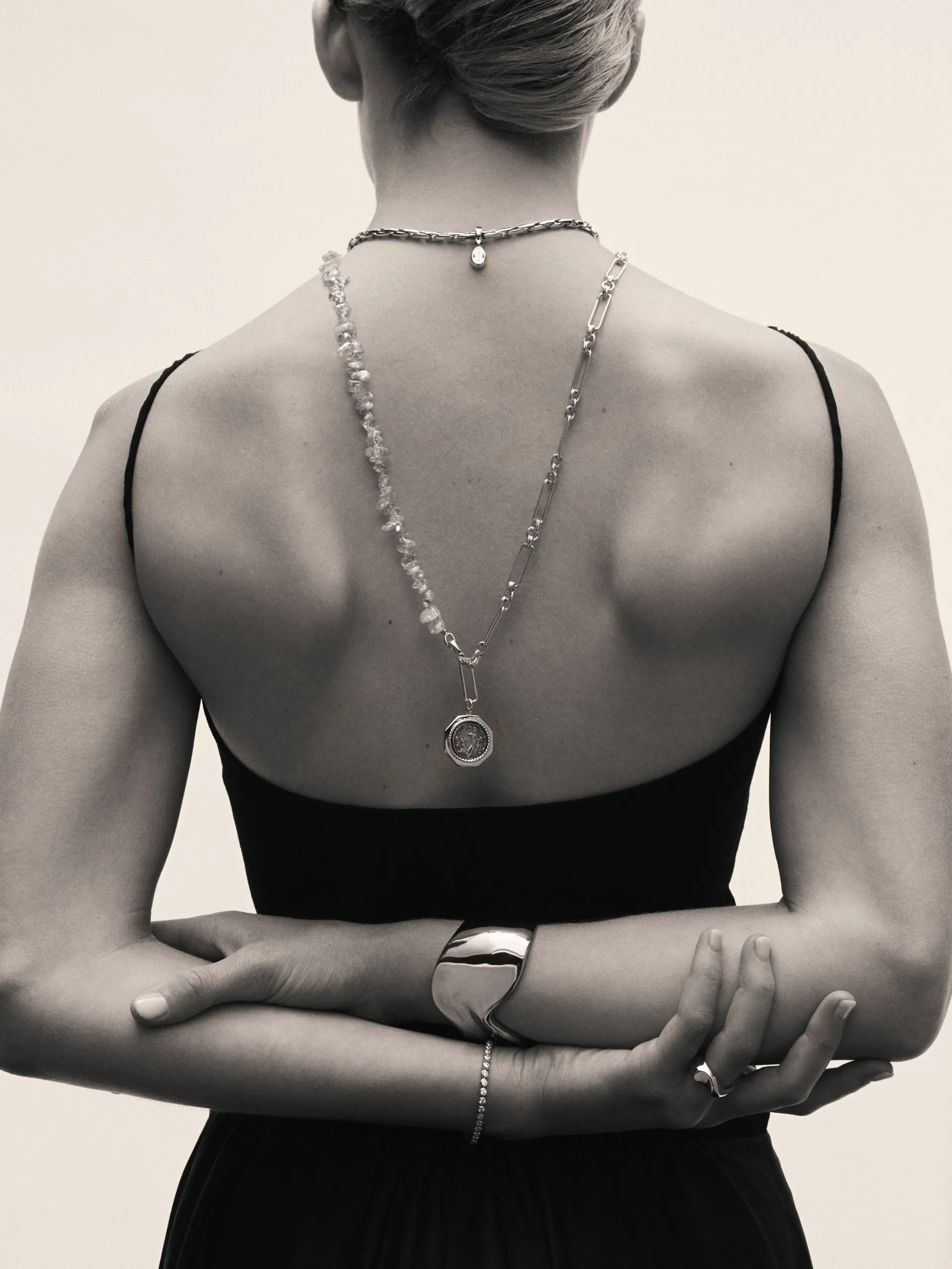 Black and white fashion photo of woman’s back wearing layered necklaces, pendant, bracelet and cuff bangle