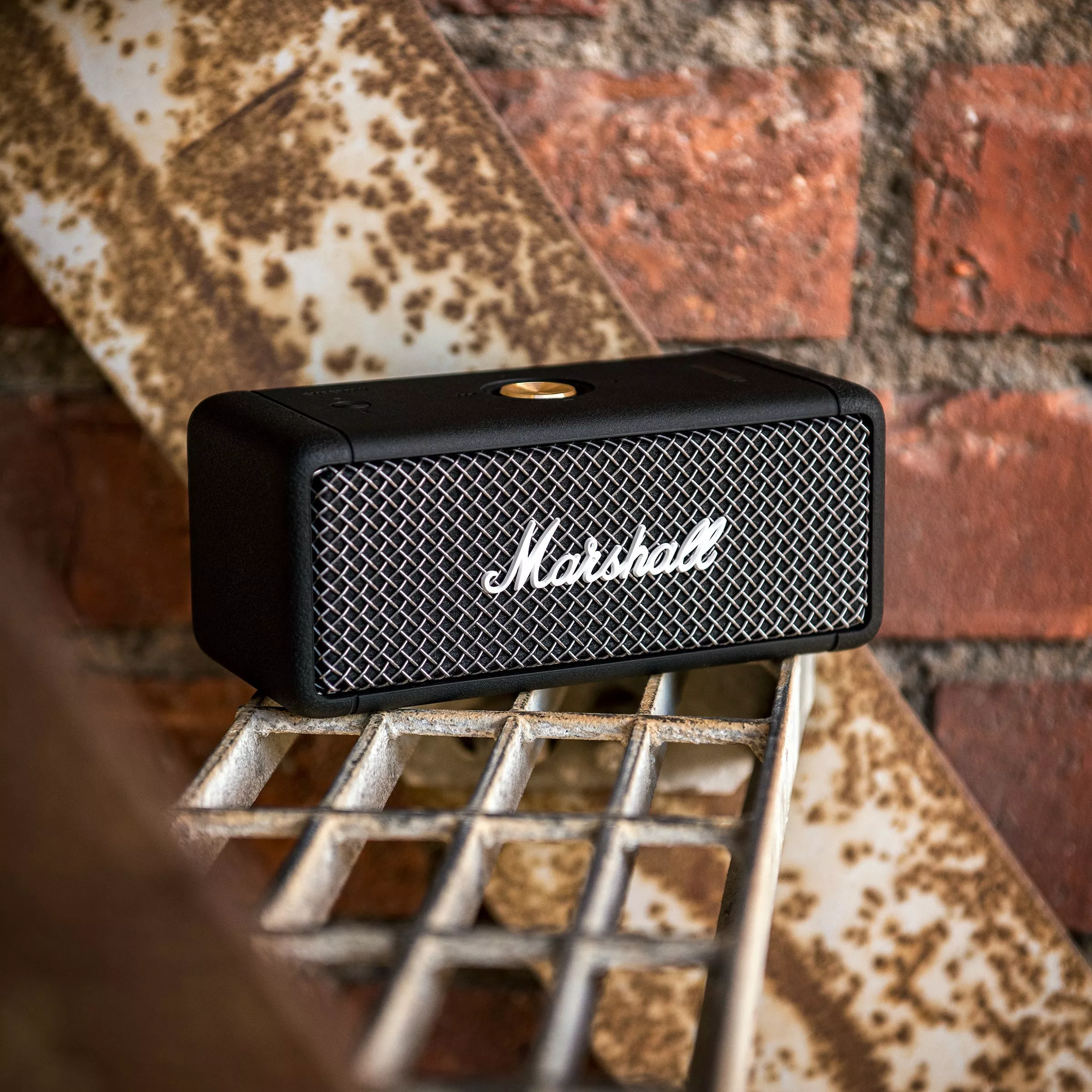 Marshall portable Bluetooth speaker on rustic metal shelf, brick wall background, close-up product photo