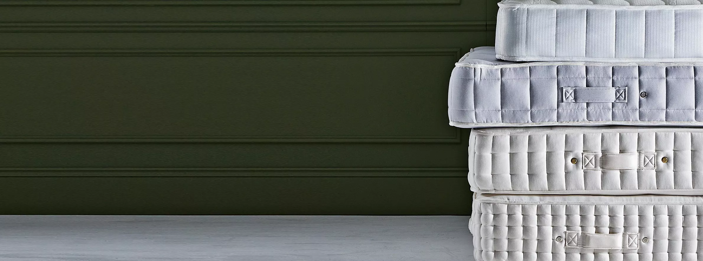 Stacked luxury pocket sprung mattresses with quilted sides and handles, set against a dark green wall backdrop