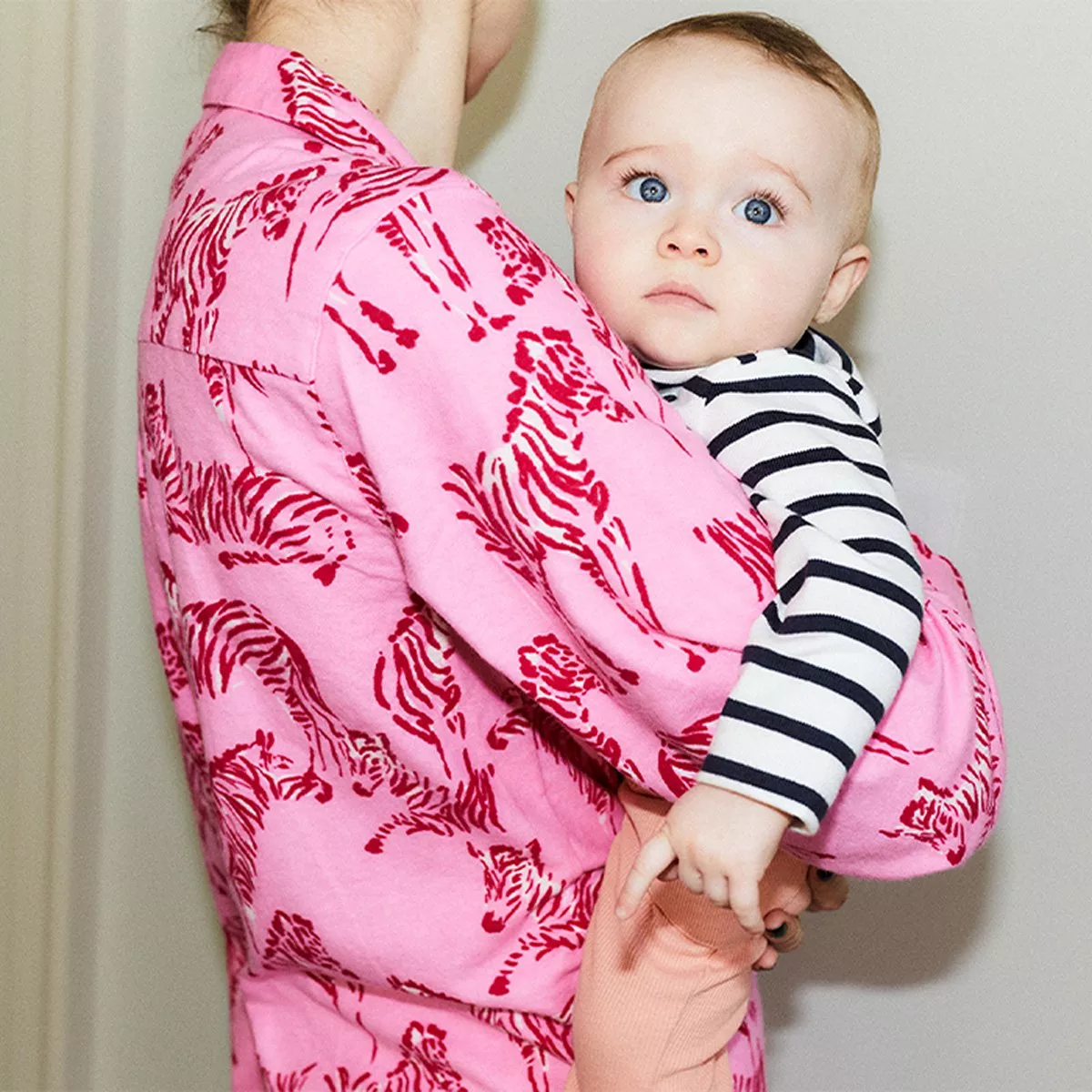 woman in a bright pink shirt with a red zebra print holding a baby who is wearing a black and white striped shirt