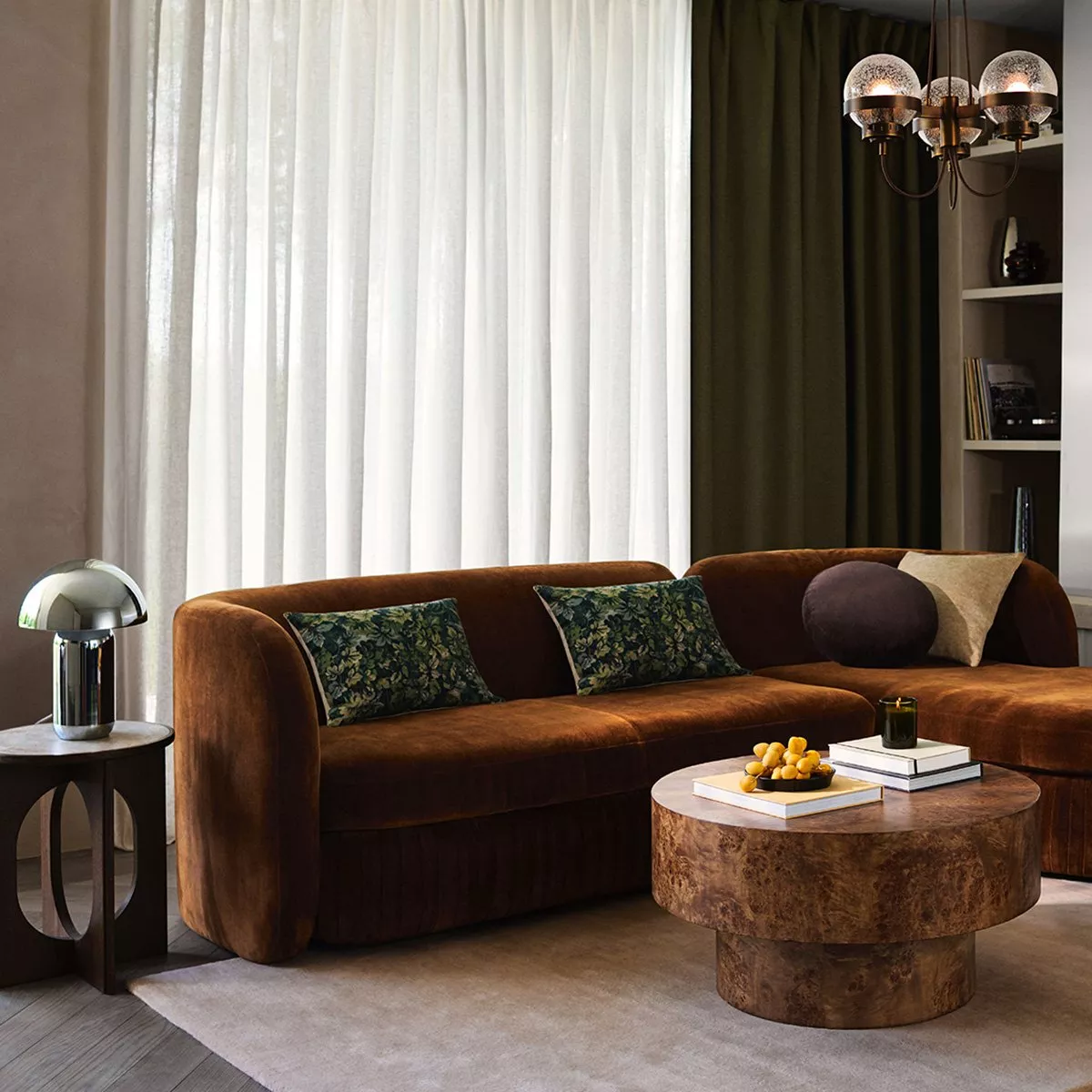 cozy, mid-century modern inspired living room featuring a velvet brown sectional sofa, a round wooden coffee table, and layered curtains in white and deep olive green
