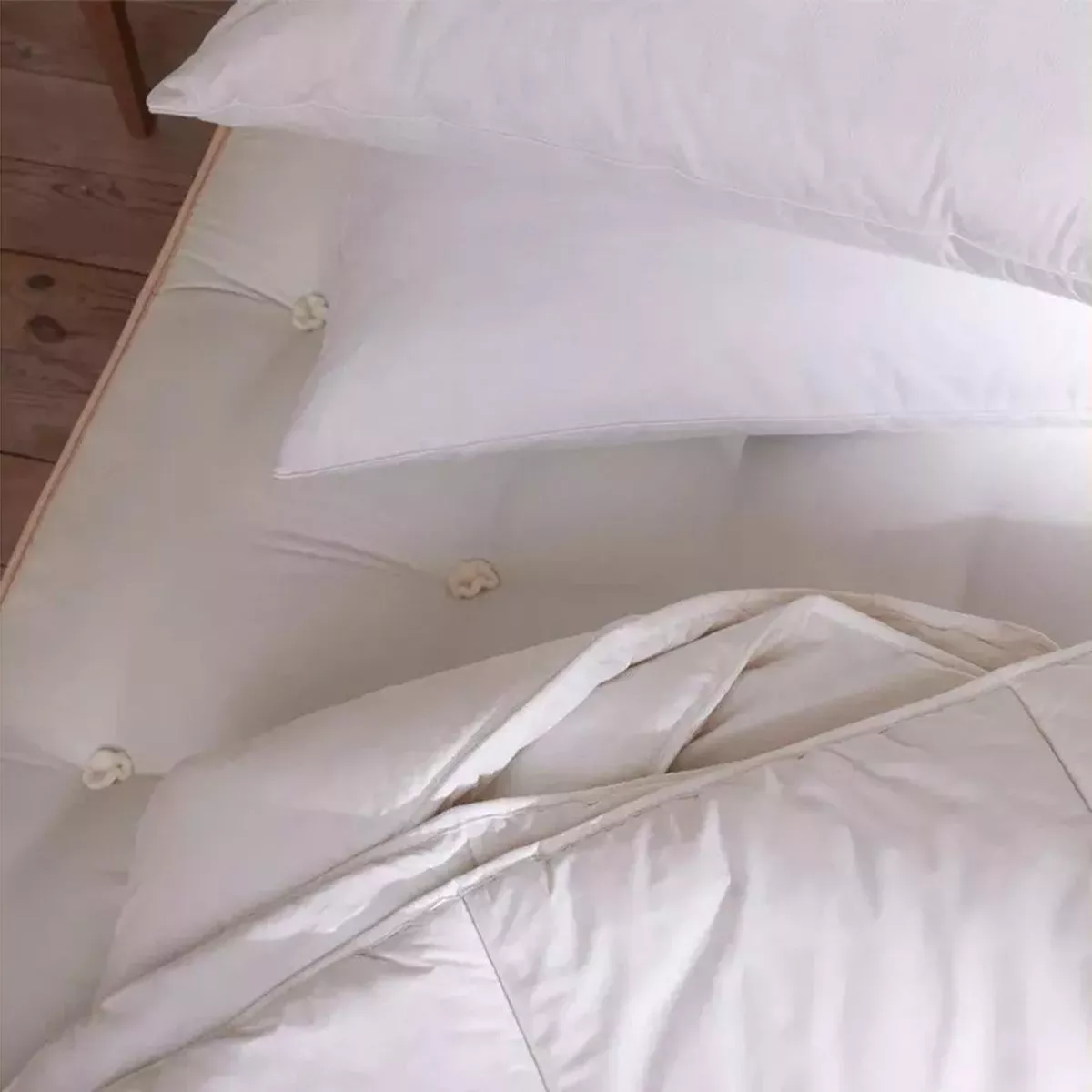 overhead close-up view of a bed featuring a white tufted mattress, white pillows, and a folded white duvet