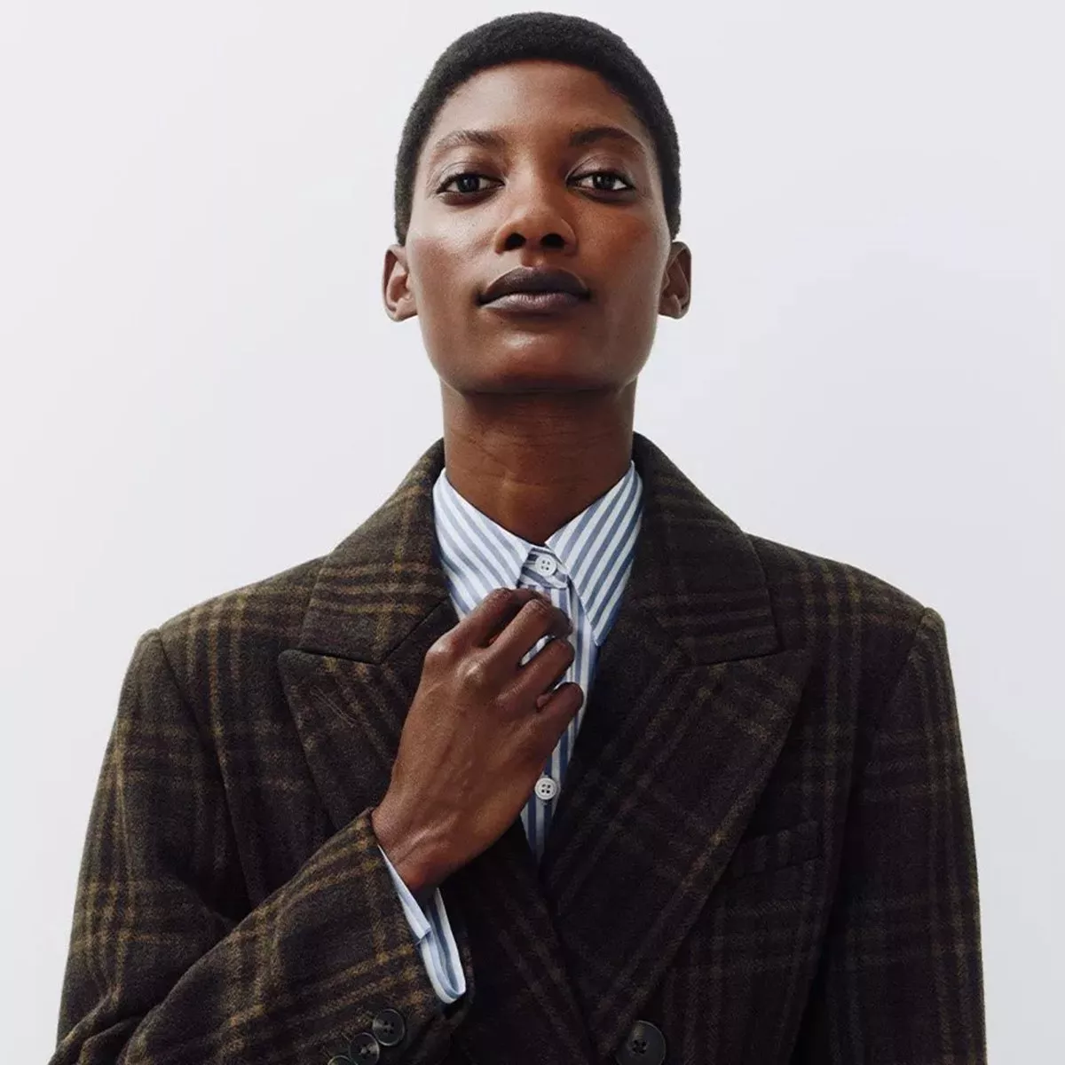 man wearing a dark, plaid double-breasted coat over a light blue and white striped button-down shirt