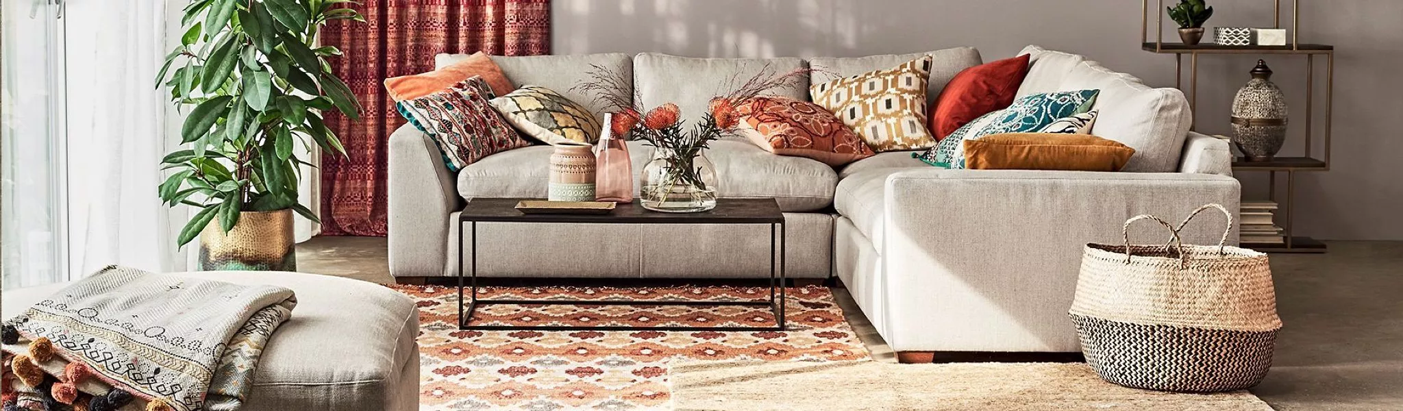 Modern cosy living room with beige sectional sofa, colourful cushions, coffee table, patterned rug and houseplant