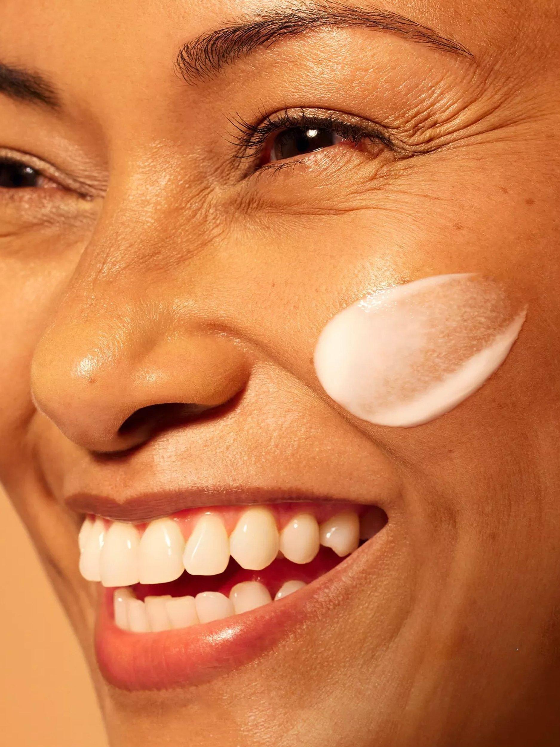 Image of a model dropping the serum on her cheek with an orange background behind her